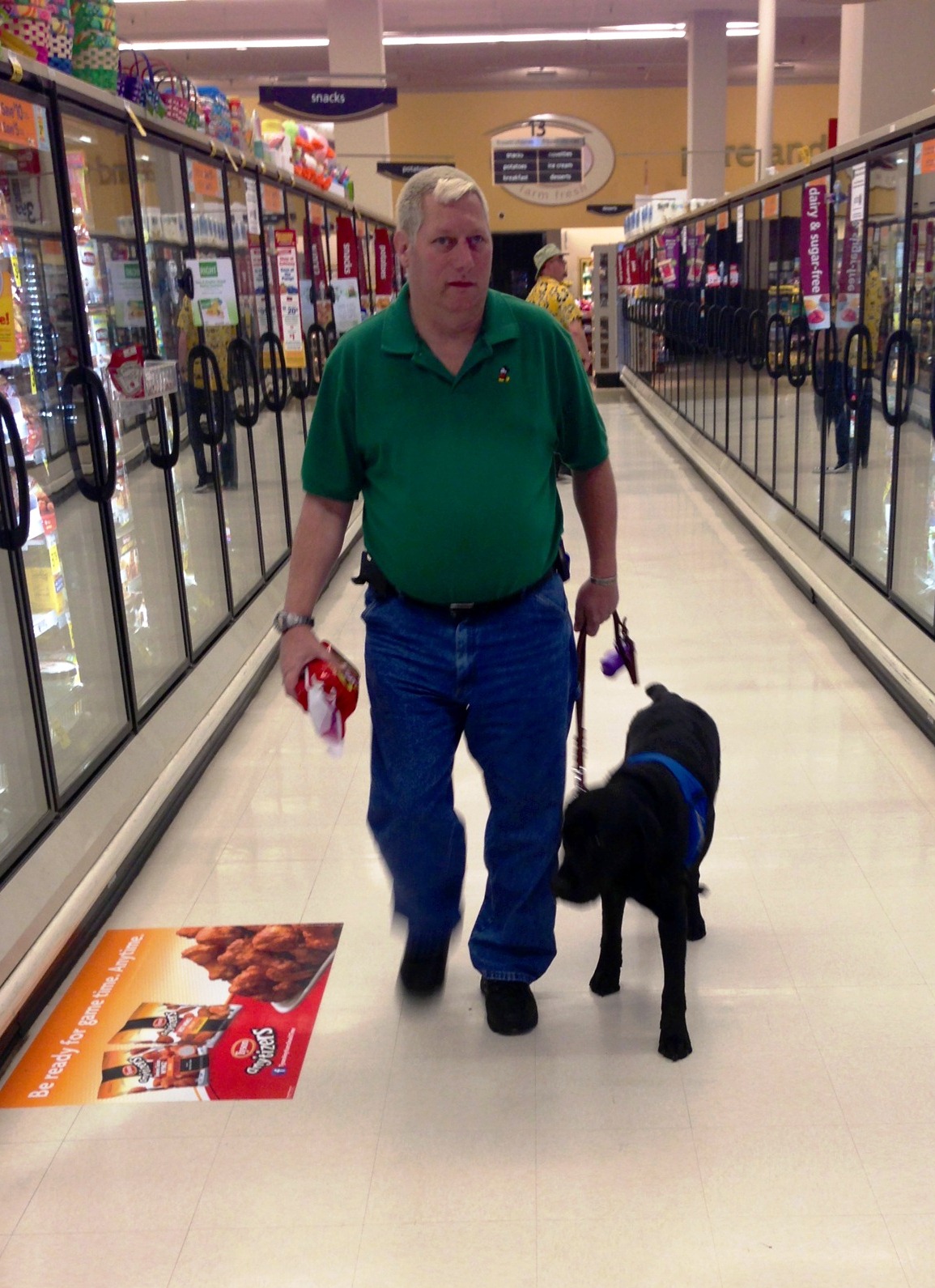 The service dog is walking along with Dennis while shopping at Safeway.